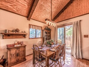 Uma sala de jantar com uma mesa de madeira posta para quatro pessoas, com cadeiras, um armário de madeira e uma estante.
