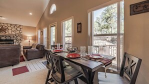A dining area with a stone fireplace, a wooden table set for four, and large windows offering a view of the outdoors.