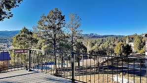 A wooden deck with a metal railing, a sign indicating an elevation of 6975, and a view of a mountainous landscape with trees. - Gray Wolf Lodge by Ruidoso Vacation Rentals (Ruidoso)