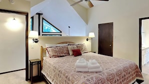 A bedroom with a large bed, two bedside lamps, a ceiling fan, and a window with a view. - Gray Wolf Lodge by Ruidoso Vacation Rentals (Ruidoso)