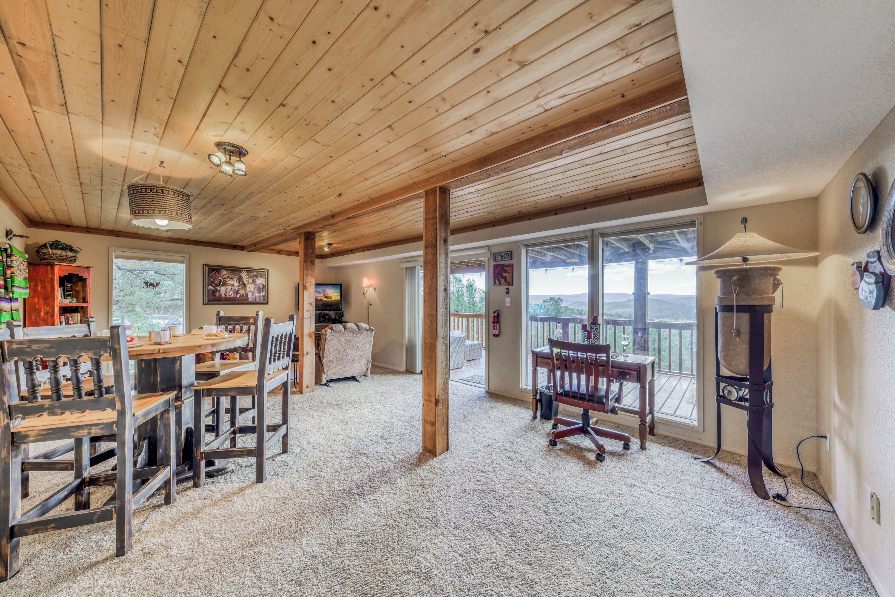 Una habitación amplia con techo de madera, un comedor con sillas y mesa de madera, un ventanal con vistas al exterior y una chimenea.