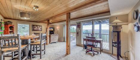Una habitación amplia con techo de madera, un comedor con sillas y mesa de madera, un ventanal con vistas al exterior y una chimenea.