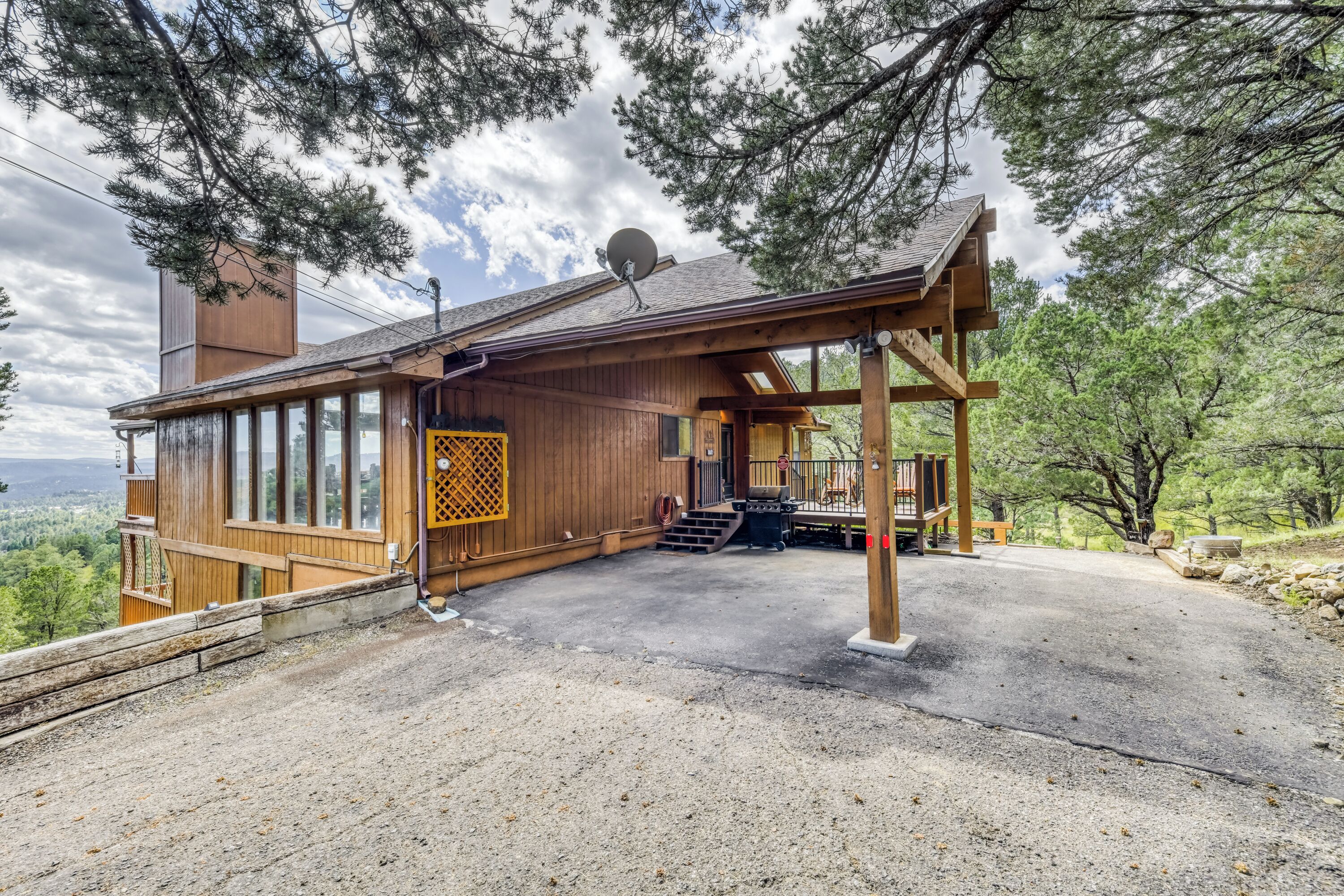 A wooden cabin with a covered porch, large windows, and a satellite dish.