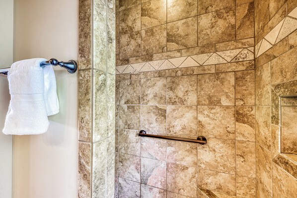 A bathroom with a towel rack holding two towels, a glass shower enclosure, and a handrail. - Living the Dream by Ruidoso Vacation Rentals (Ruidoso)