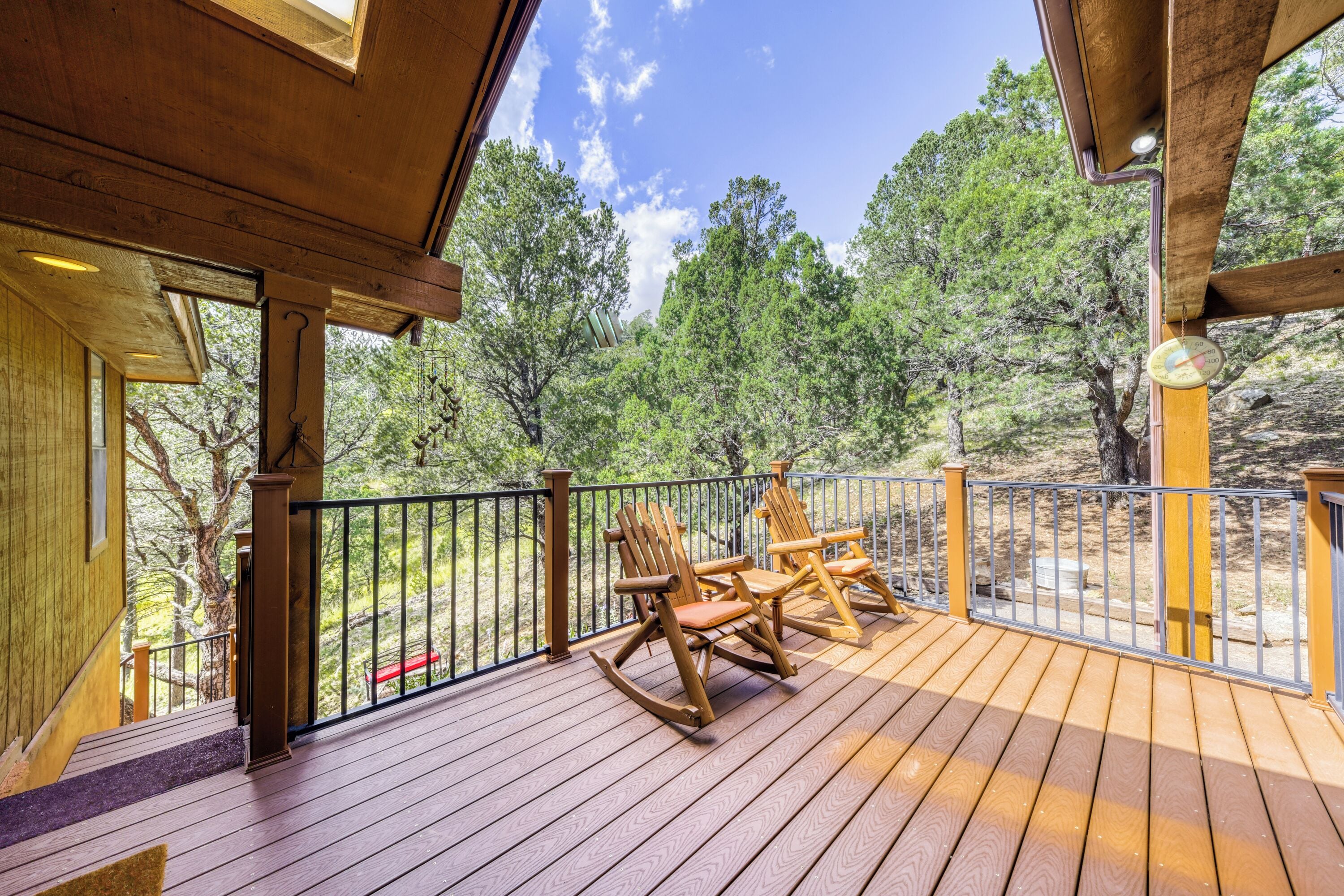 A wooden deck with rocking chairs, a railing, and a view of trees.