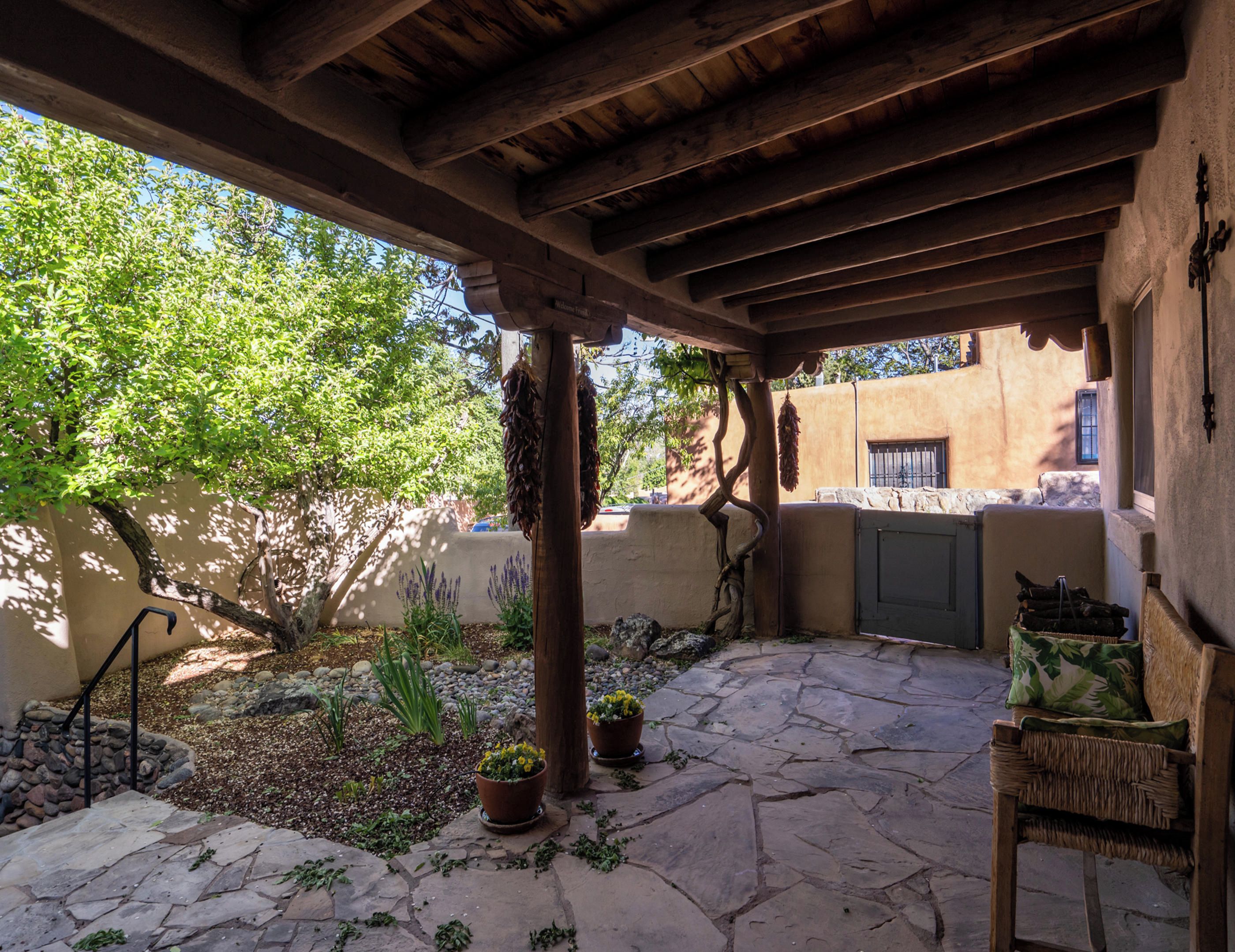 A covered patio with stone flooring, potted plants, and a wicker chair.