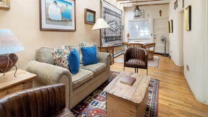 Un salón acogedor con un sofá, sillón y mesa de centro. Cuenta con un comedor con una mesa y sillas, y una puerta que da a otra habitación.