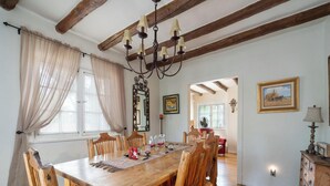 Un comedor con mesa y sillas de madera, una araña y vistas de la habitación contigua.