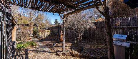A covered outdoor area with a barbecue grill, a wooden pergola, and a rustic fence.