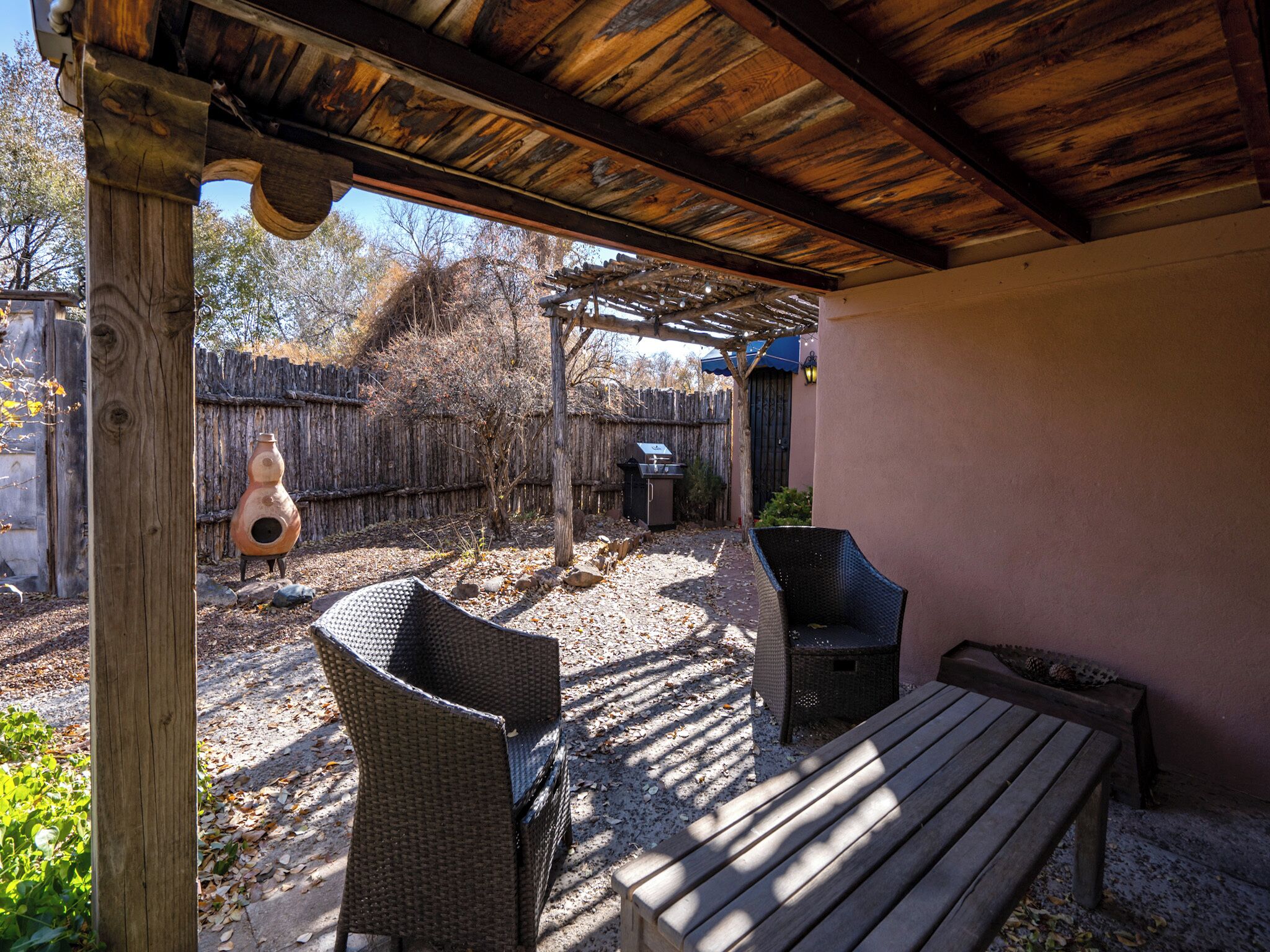 Une terrasse extérieure aménagée avec des meubles en osier, un banc en bois et un barbecue.
