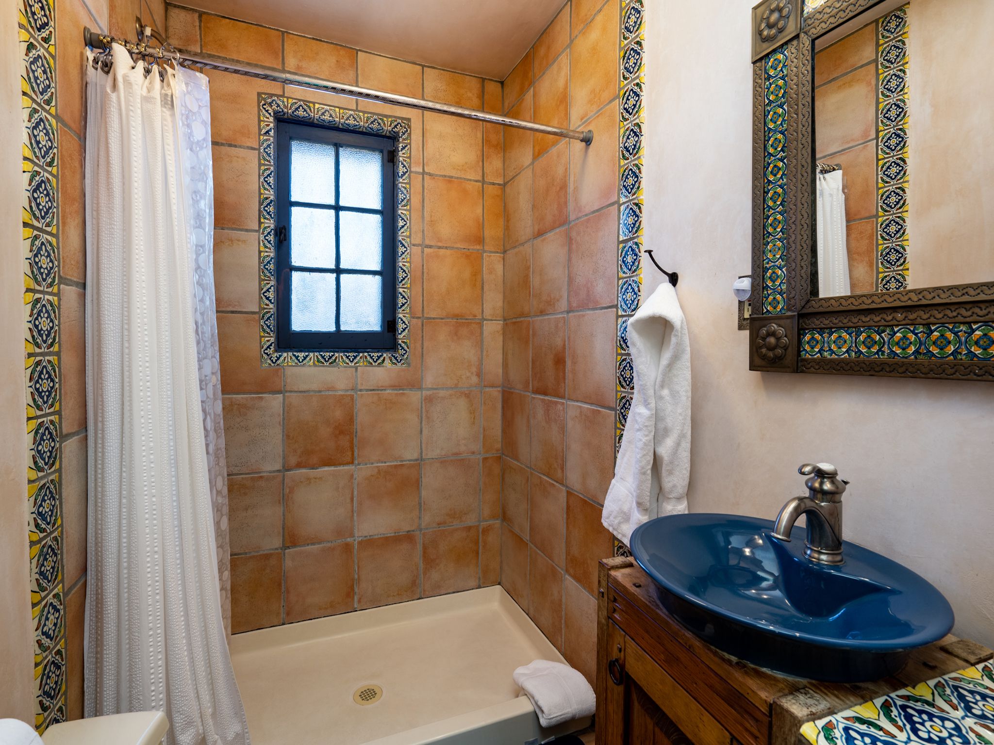 Un baño con bañera, un lavamanos azul, una ventana con marco decorativo y un perchero para toallas.