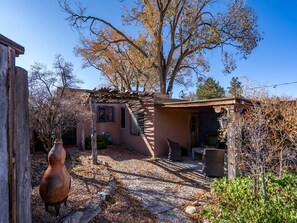 A rustic house with a stone pathway leading to a wooden door. - La Vida Buena by Kokopelli Property Management (Santa Fe)