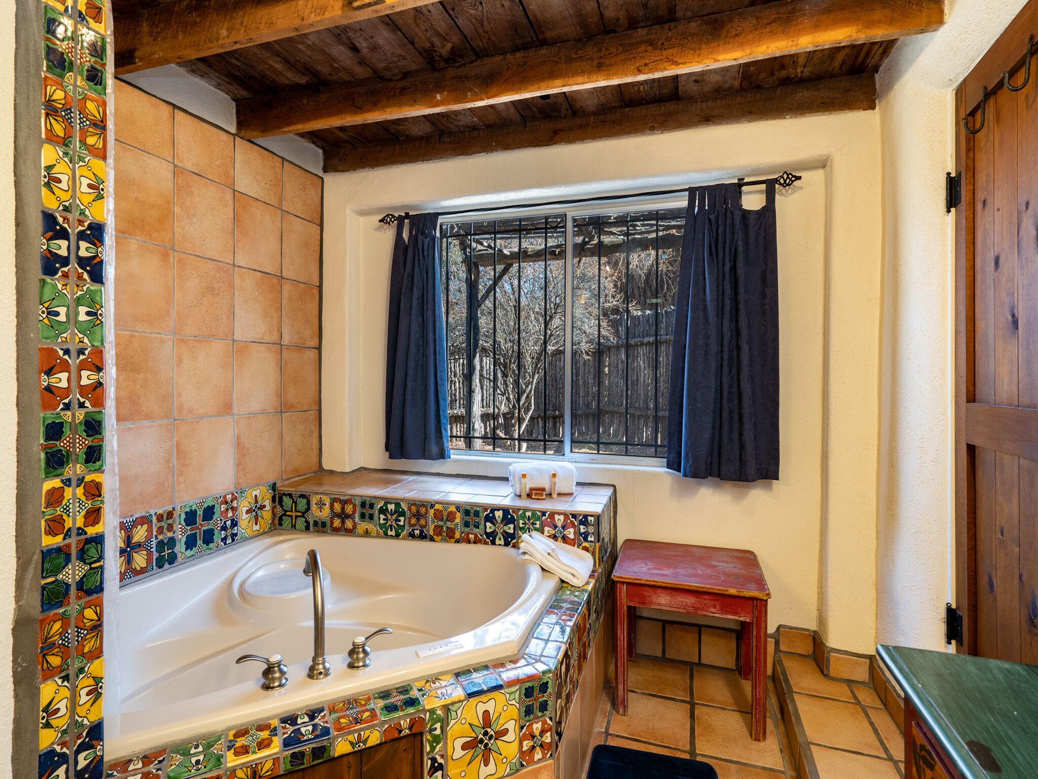 A bathroom with a bathtub, a window with curtains, and a wooden bench.