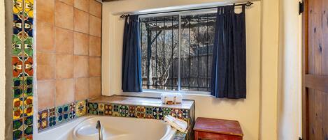 A bathroom with a bathtub, a window with curtains, and a wooden bench.