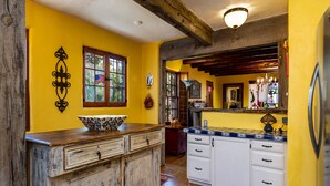 A kitchen with wooden cabinets, a large window with an American flag, and a colorful rug. - La Vida Buena by Kokopelli Property Management (Santa Fe)