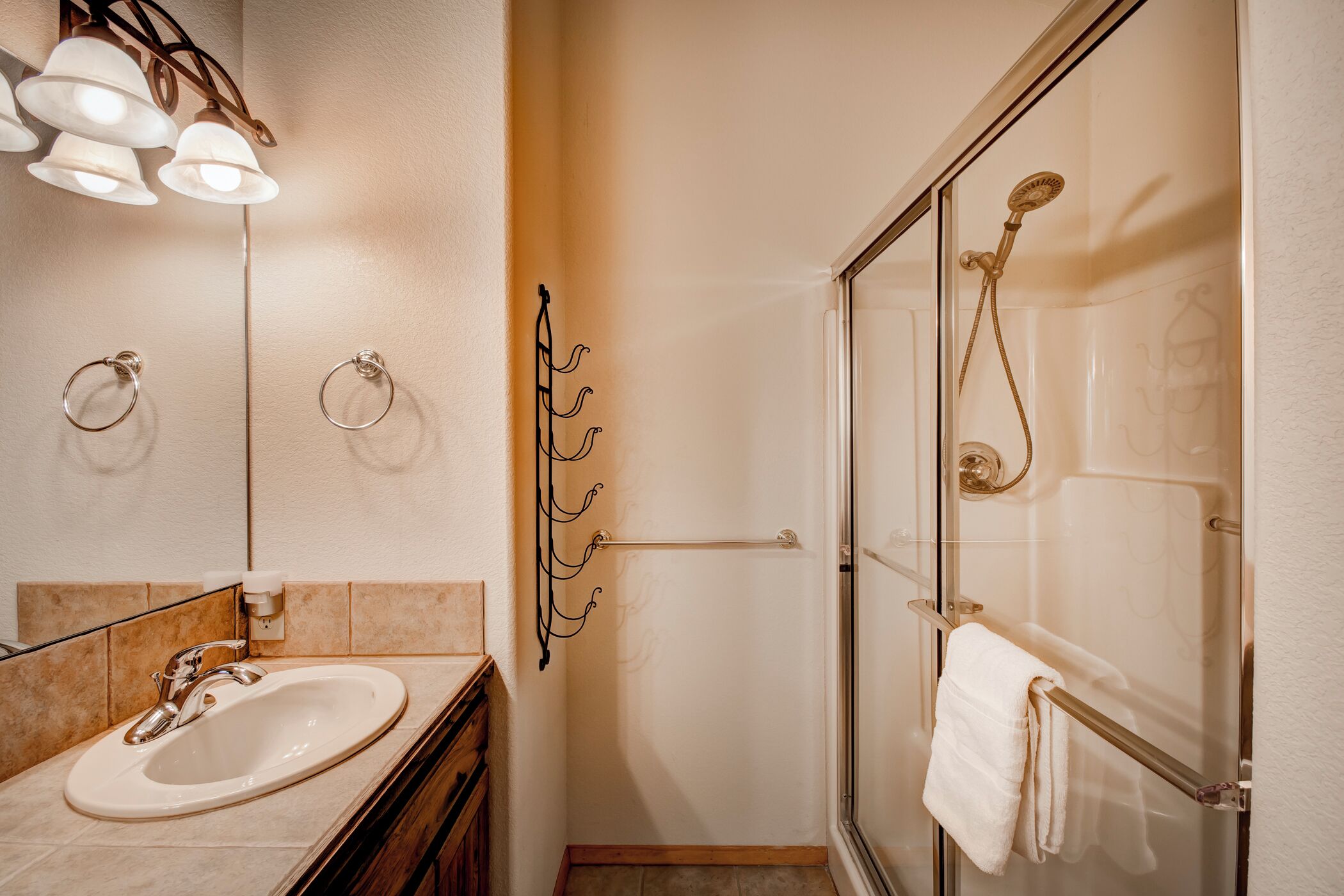 A bathroom with a sink, mirror, towel rack, and glass-enclosed shower.