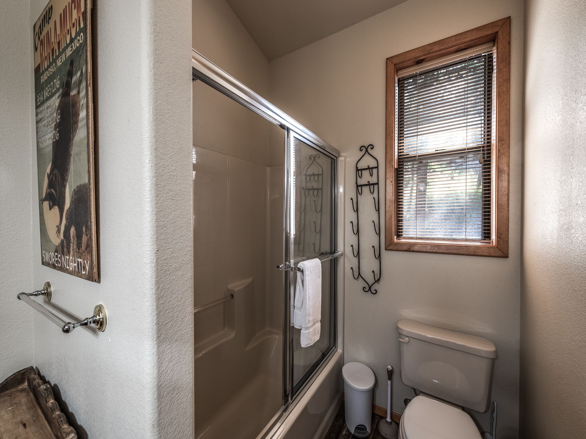 Ein Badezimmer mit Duschkabine, Toilette, Fenster mit Jalousien und Handtuchhalter.