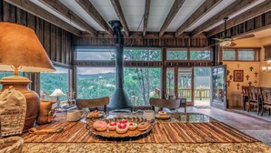 A spacious room with a large window, a fireplace, and a dining area with a table set for a meal. - Neeley Mountain House by Ruidoso Vacation Rentals (Alto)