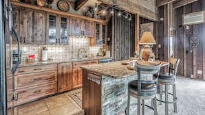 A rustic kitchen with wooden cabinets, a tiled backsplash, and a central island with stools. - Neeley Mountain House by Ruidoso Vacation Rentals (Alto)
