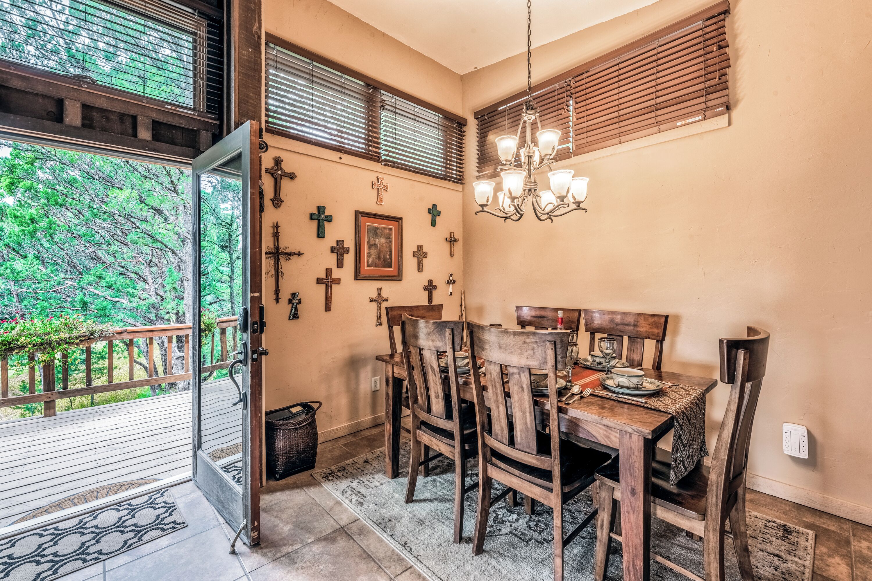 A dining area with a wooden table and chairs, a chandelier, and multiple crosses on the wall.