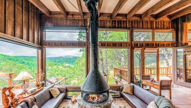 A cozy room with a stone fireplace, comfortable seating, and large windows offering a view of the outdoors. - Neeley Mountain House by Ruidoso Vacation Rentals (Alto)