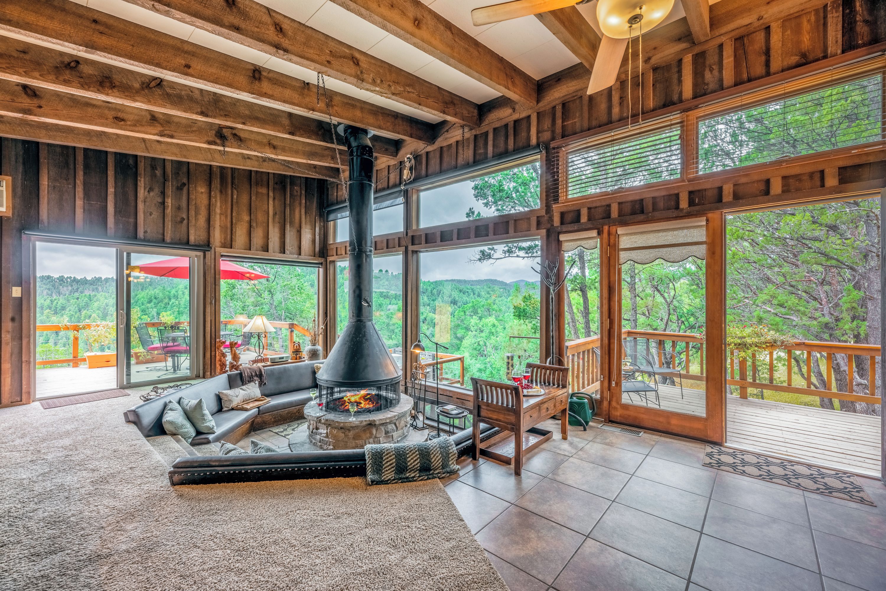 A spacious living area with a stone fireplace, large windows, and a wooden ceiling.