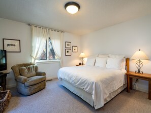 Quarto de hotel com uma cama grande, uma cadeira, uma televisão e uma janela com cortinas.