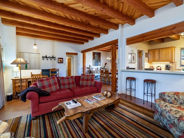 A cozy living room with a red sofa, wooden coffee table, and striped rug. - Puertas de Canyon Road by Kokopelli Property Management (Santa Fe)