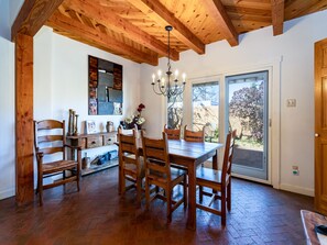 Uma sala de jantar com mesa e cadeiras de madeira, um candelabro e vista através de uma porta de vidro.