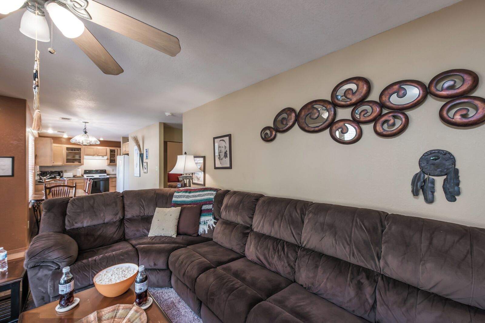 A living room with a brown sectional sofa, a ceiling fan, and wall art.