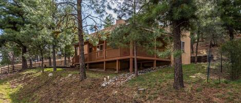 A cabin with a wooden deck, surrounded by pine trees, set on a hillside.