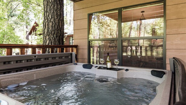 Un jacuzzi con dos copas de vino y una botella, rodeado de un muelle de madera y árboles.