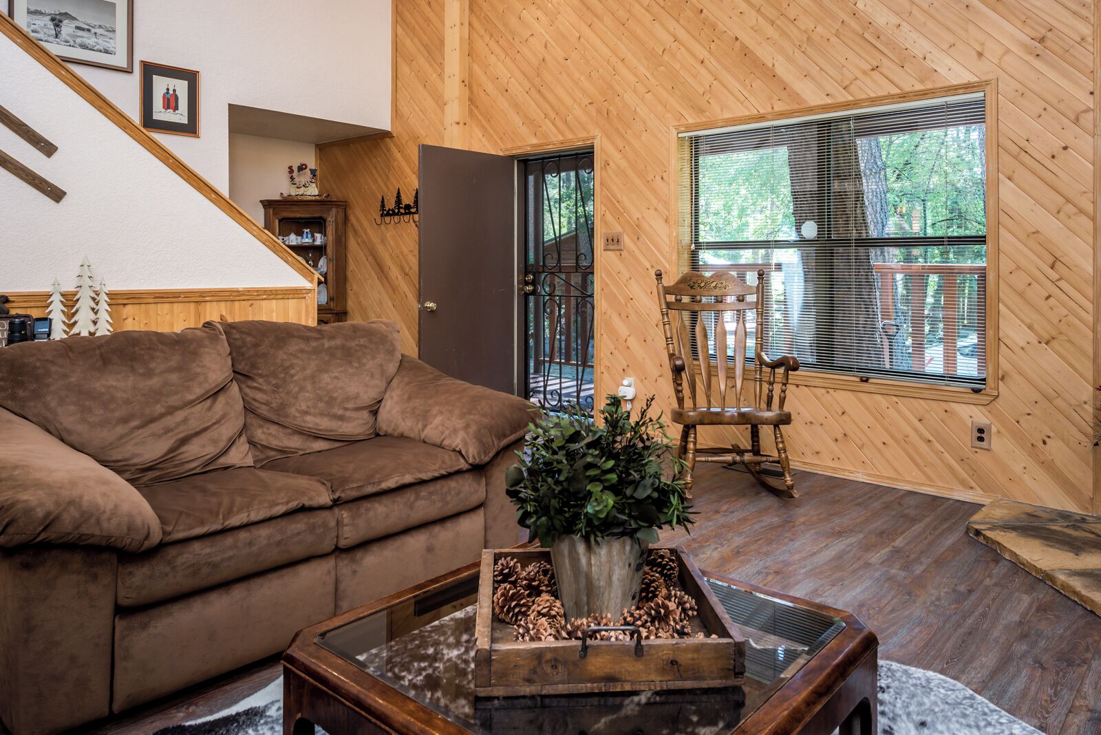 A cozy living room with a brown sofa, a wooden coffee table with pinecones, and a window with blinds.