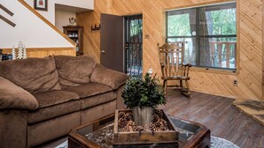 Un salón acogedor con un sofá marrón, una mesa de centro de madera con piñas, y una ventana con persianas.