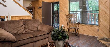 A cozy living room with a brown sofa, a wooden coffee table with pinecones, and a window with blinds.