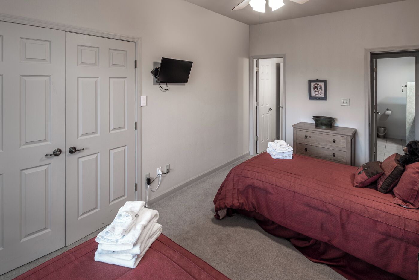A bedroom with a bed, a dresser, a TV mounted on the wall, and a door.