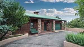A rustic log cabin with a green metal roof, stone pillars, and a green swing bench outside. - Robins Nest by Ruidoso Vacation Rentals (Ruidoso)