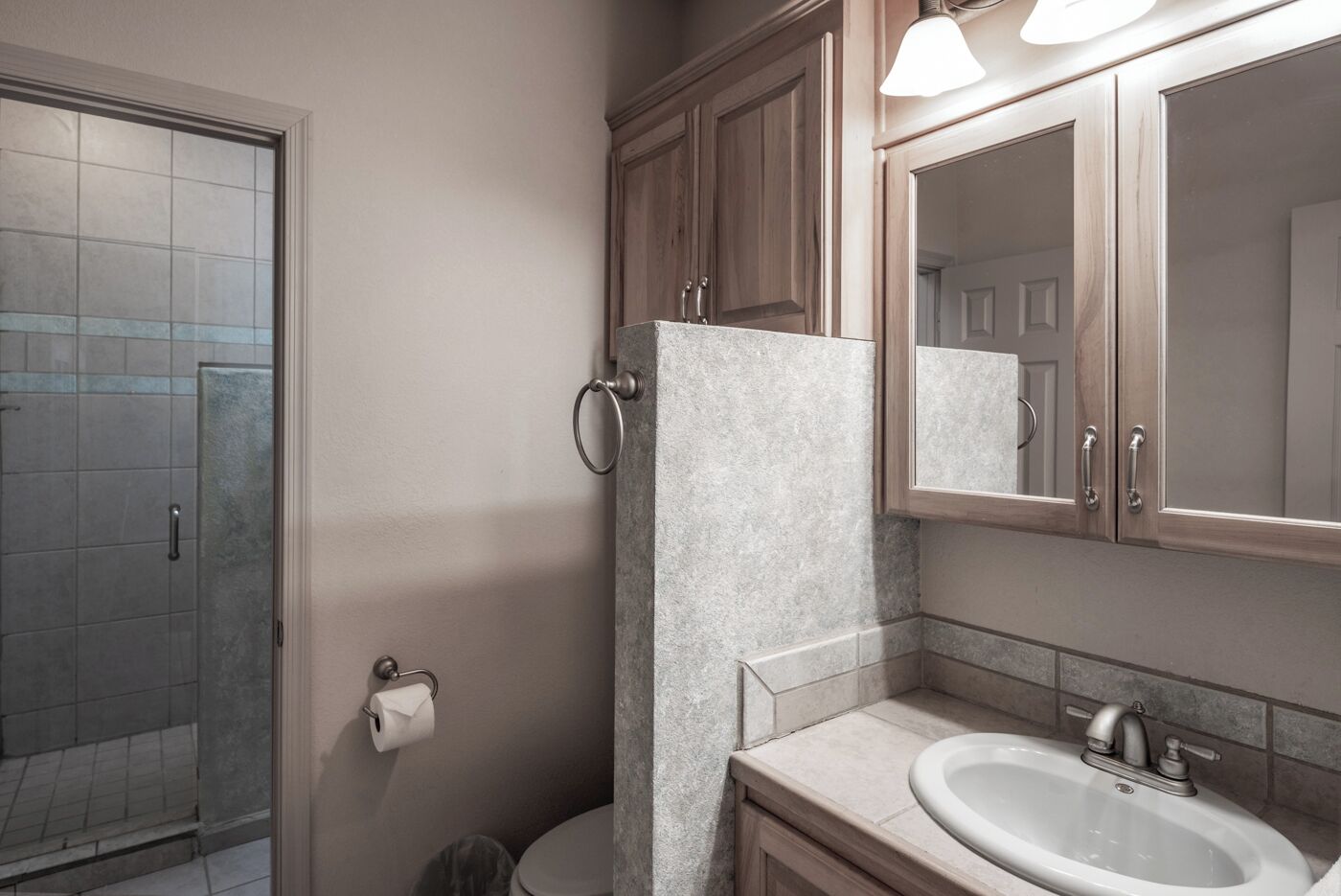 A bathroom with a shower, toilet, sink, and wooden cabinets.