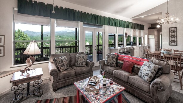 A spacious living room with two sofas, a coffee table, and a dining area with a chandelier. Large windows offer a view of the mountains. - Robins Nest by Ruidoso Vacation Rentals (Ruidoso)
