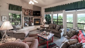A cozy living room with a fireplace, comfortable seating, and large windows offering a view of the outdoors. - Robins Nest by Ruidoso Vacation Rentals (Ruidoso)