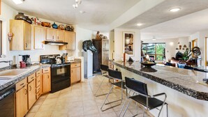 A spacious kitchen with wooden cabinets, a granite countertop, and a central island with bar stools. - Sunlit Hills Art and Views by Kokopelli Property Management (Santa Fe)