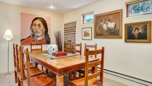 A dining area with a wooden table and chairs, surrounded by framed artworks and a large painting. - Sunlit Hills Art and Views by Kokopelli Property Management (Santa Fe)