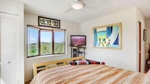 A bedroom with a bed, a television, and a view of the outdoors. - Sunlit Hills Art and Views by Kokopelli Property Management (Santa Fe)
