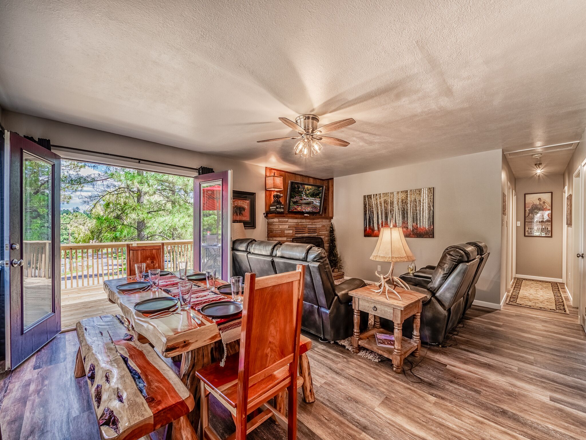 A spacious living area with a wooden dining table, leather seating, a fireplace, and a balcony with a view of trees.