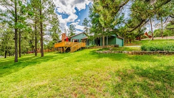 A house with a wooden deck, a stone wall, and a grassy yard with trees.