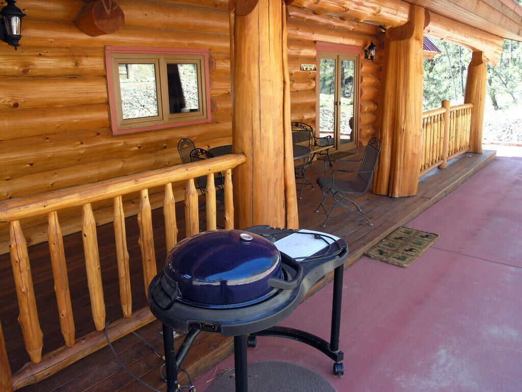 A wooden cabin with a covered porch, a grill, and a dining area with chairs and a table.