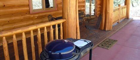 A wooden cabin with a covered porch, a grill, and a dining area with chairs and a table.
