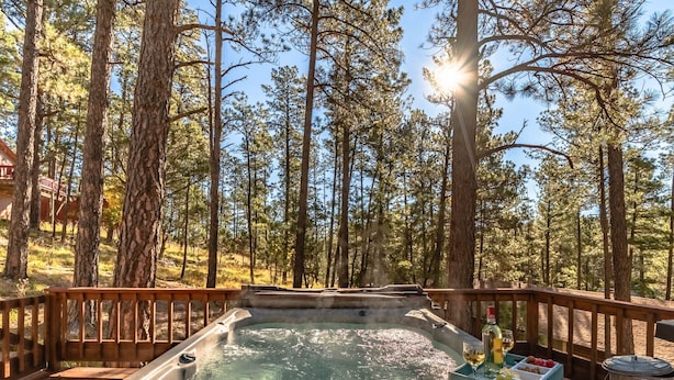 Ein Whirlpool auf einer Holzterrasse, umgeben von hohen Kiefern, mit blauem Himmel und durchschimmerndem Sonnenlicht.