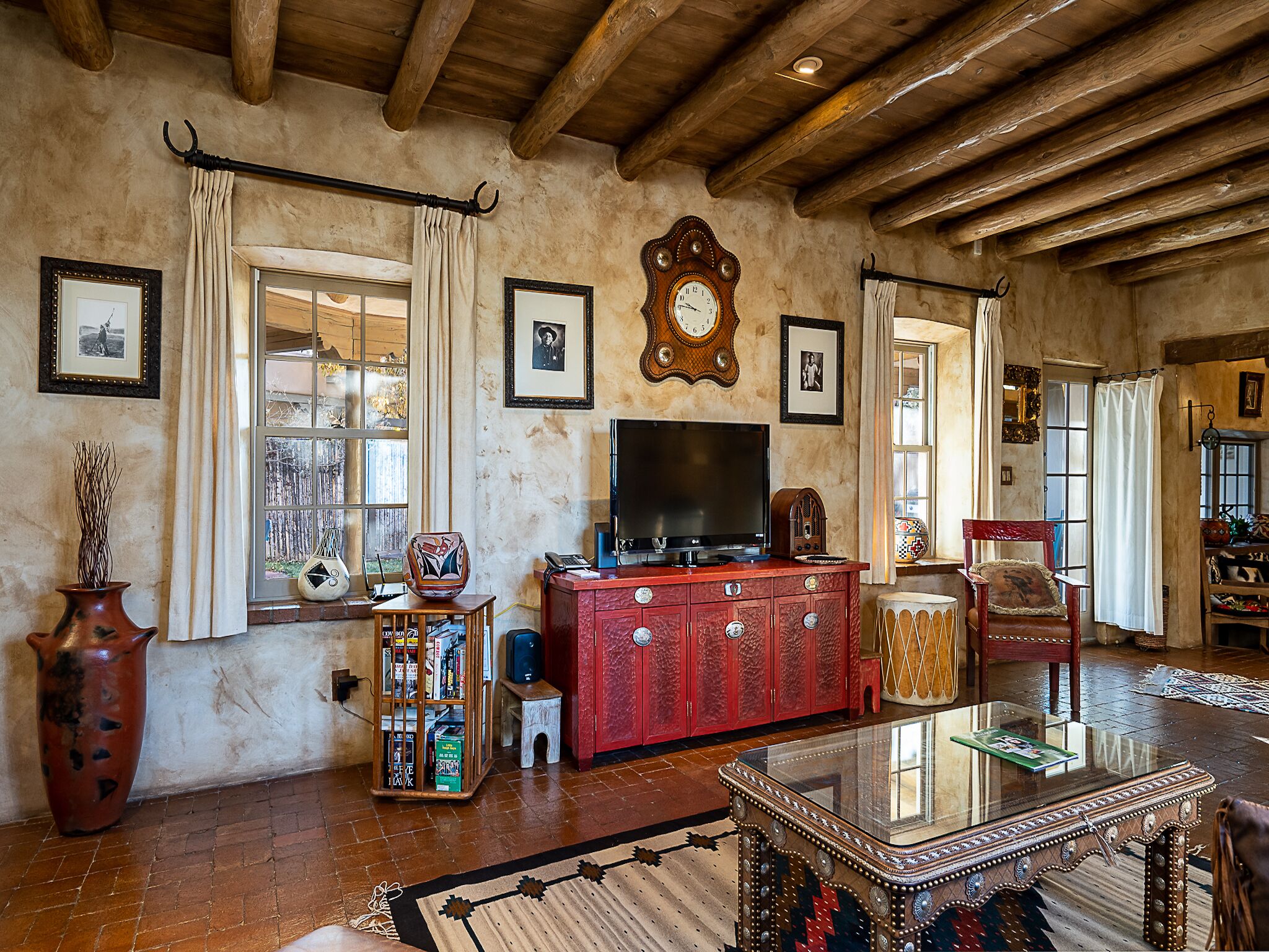 A rustic living room with exposed wooden beams, a red entertainment unit, a large clock, and a television.