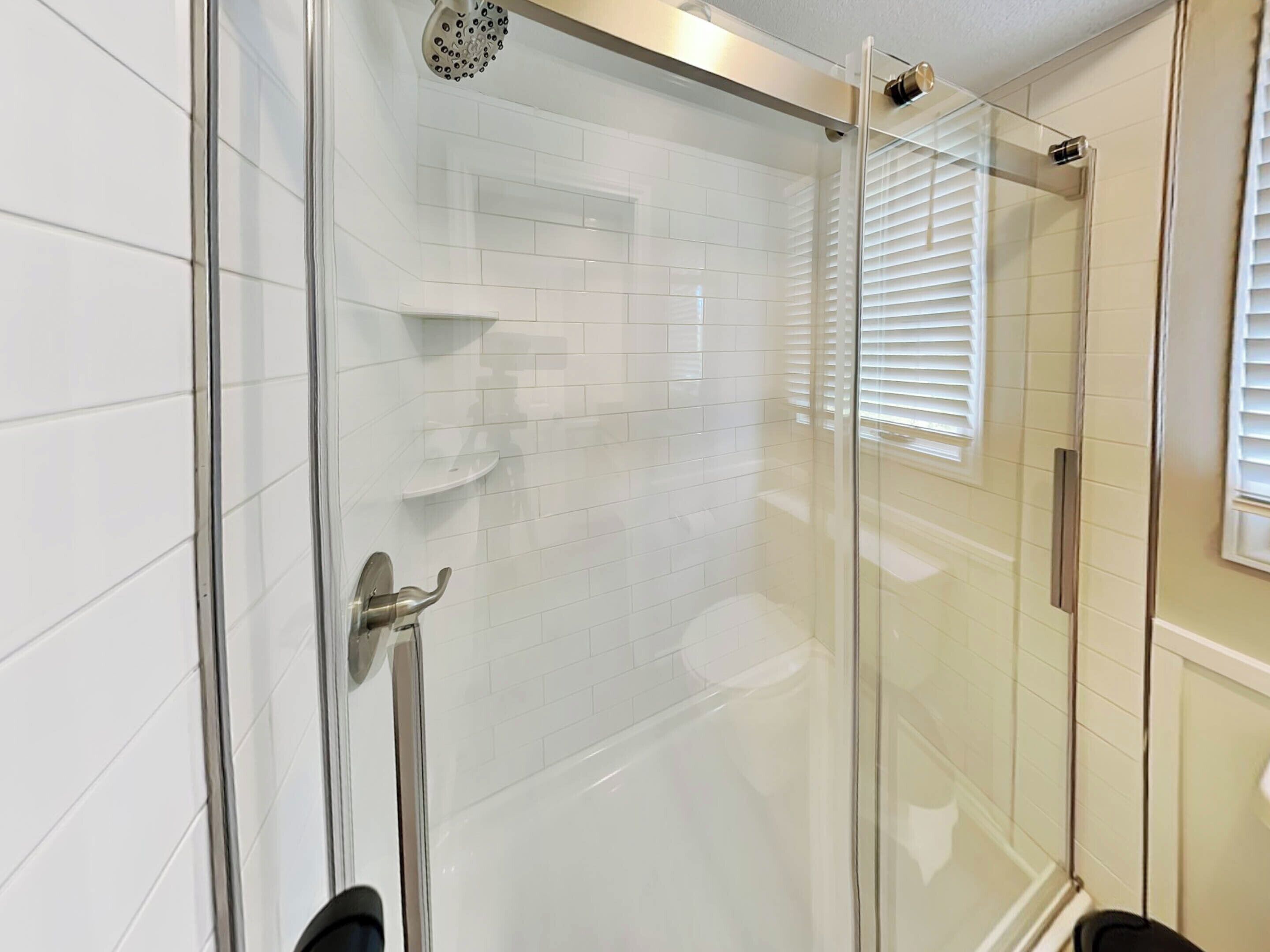 A glass-enclosed shower with white tiles and a glass door.